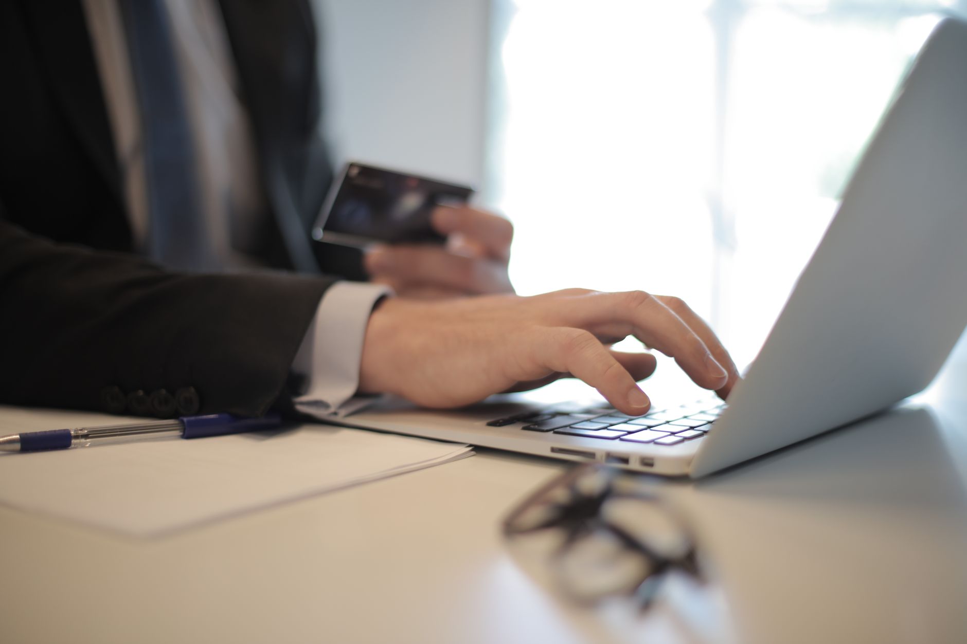 Une personne utilise une carte bancaire devant le clavier d’un ordinateur portable sur un bureau.